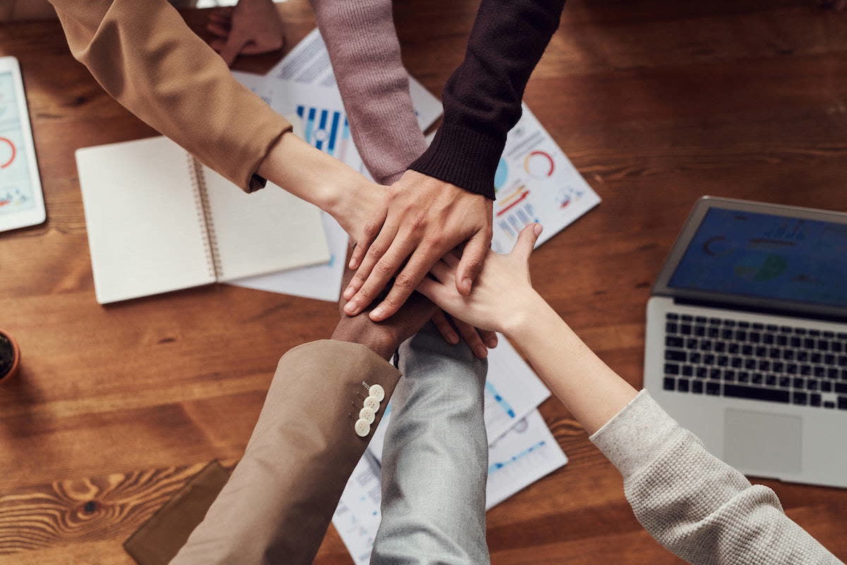 A team places their hands together over a shared workspace.